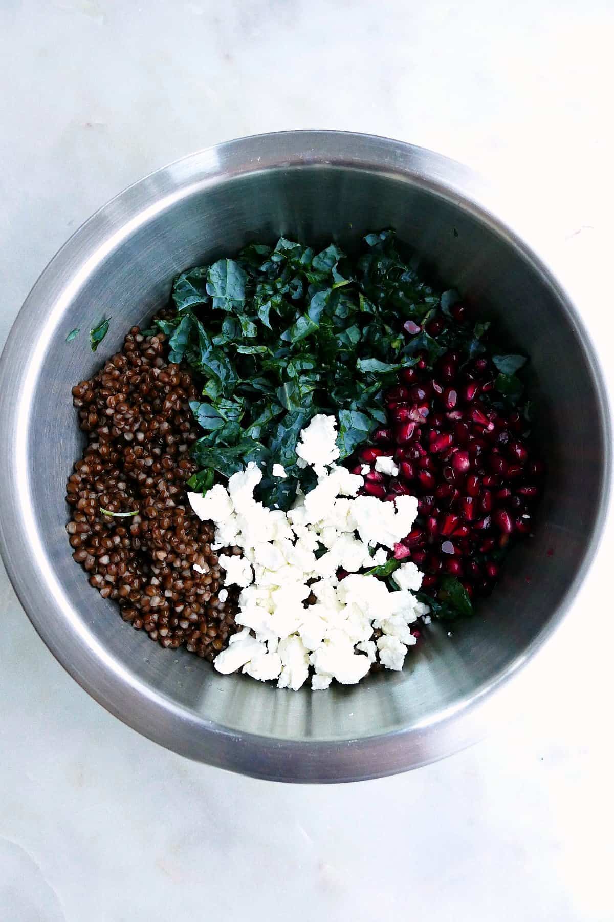 black lentils, finely chopped kale, goat cheese crumbles, and pomegranate arils in a bowl