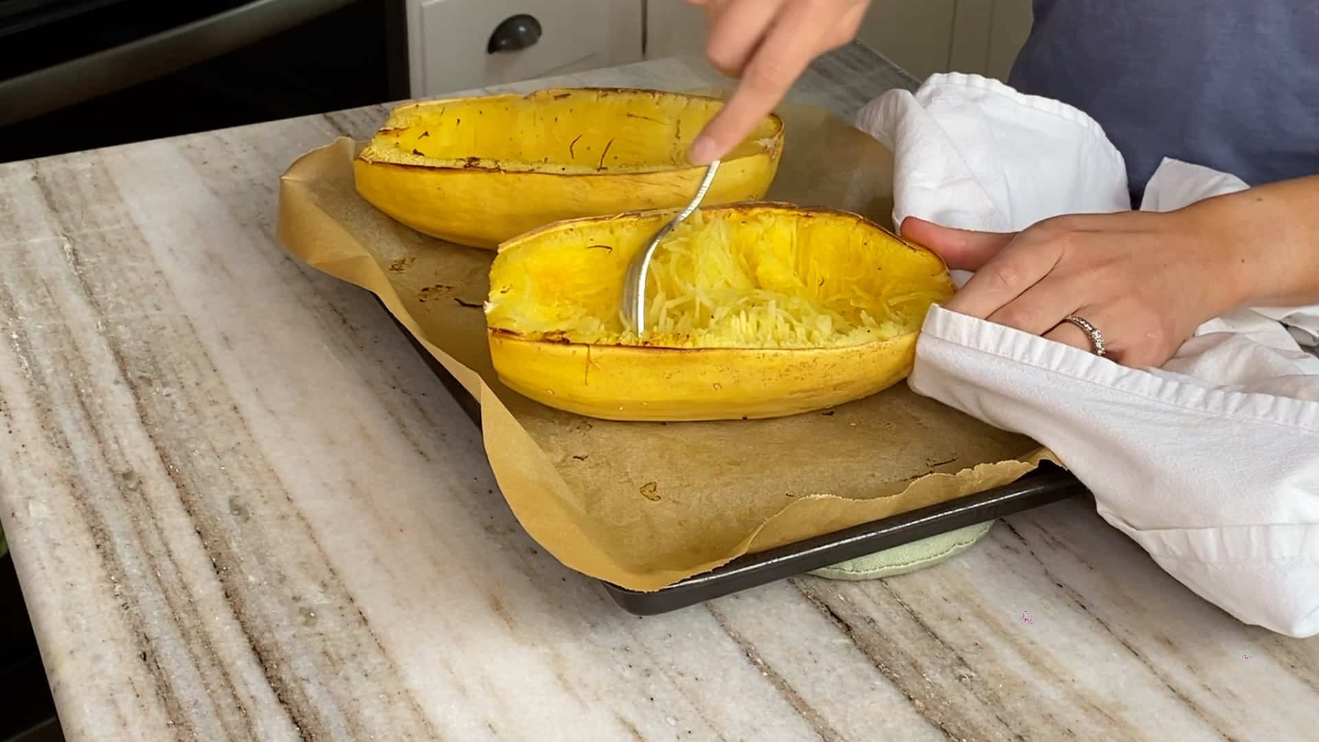 woman loosening spaghetti squash noodles with a fork over a baking sheet
