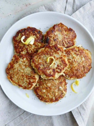 square image of six kohlrabi fritters topped with lemon zest on a serving platter