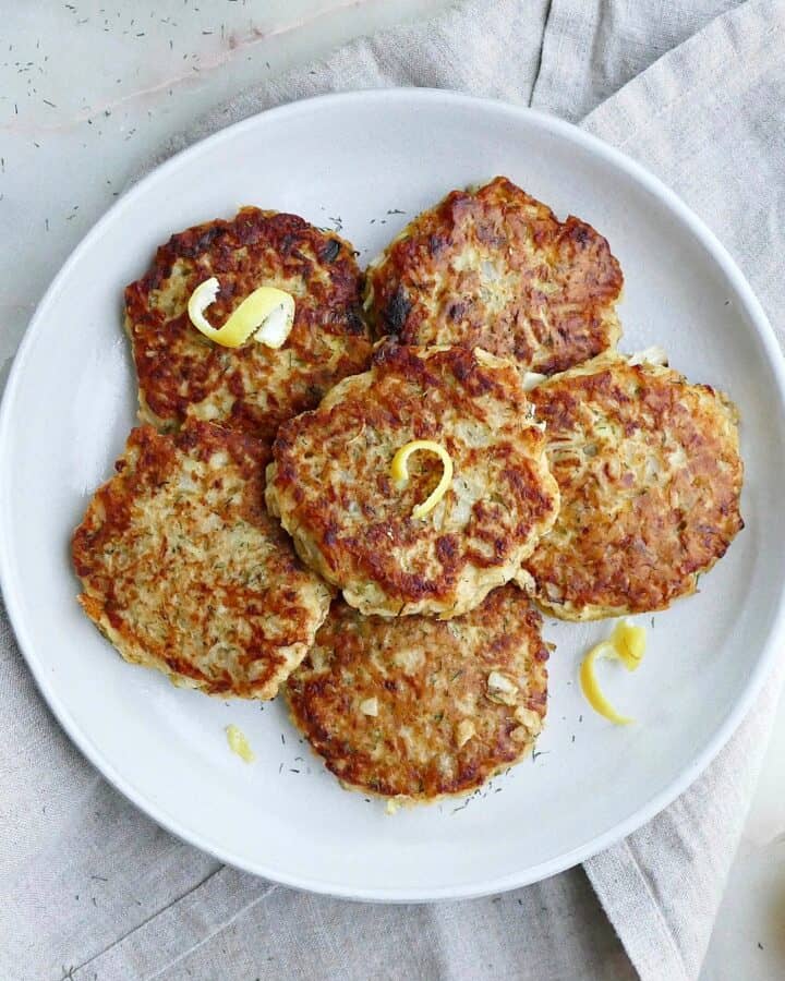 square image of six kohlrabi fritters topped with lemon zest on a serving platter