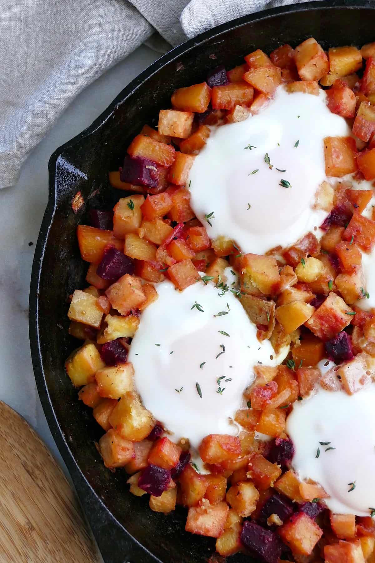 close-up of root vegetable hash with eggs in a skillet on a counter