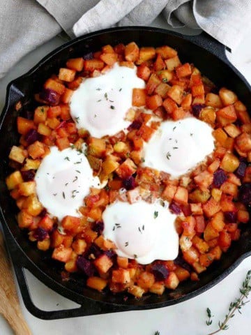 square image of root vegetable hash topped with four eggs in a skillet