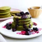 stack of spinach pancakes with berry compote on a plate in front of more pancakes