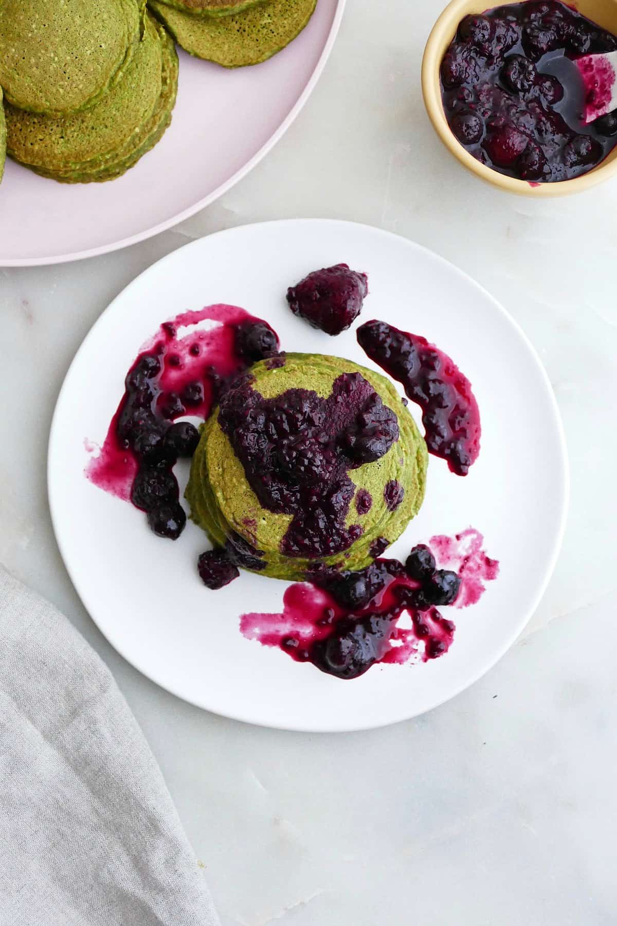 overhead image of a stack of green pancakes with berry compote