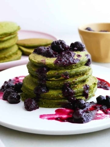 square image of a stack of green pancakes with berry compote on a plate