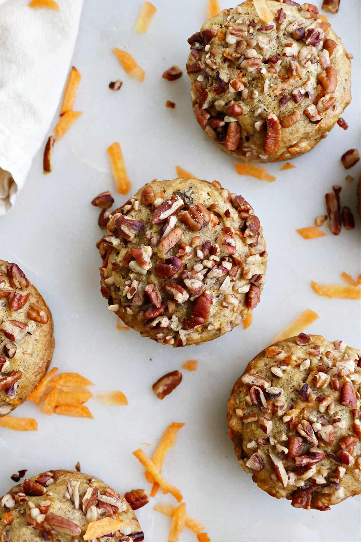 banana carrot muffins on a counter next to shredded carrots and pecans