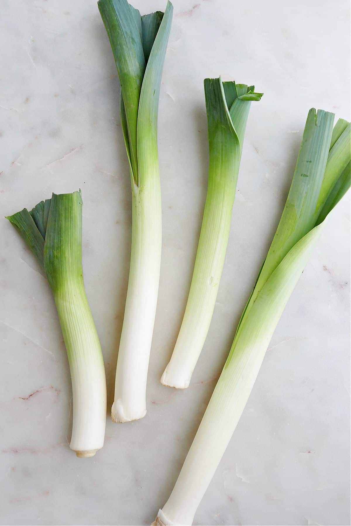 four leeks spread out next to each other on a simple white countertop