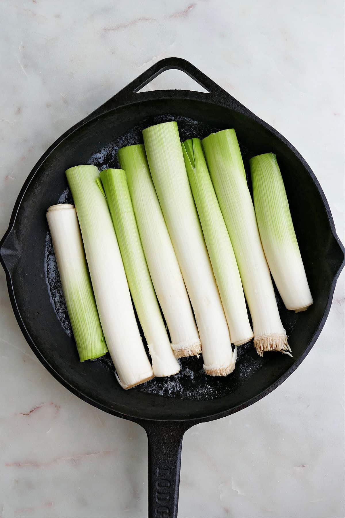 leeks sliced lengthwise snuggled next to each other in a cast iron skillet