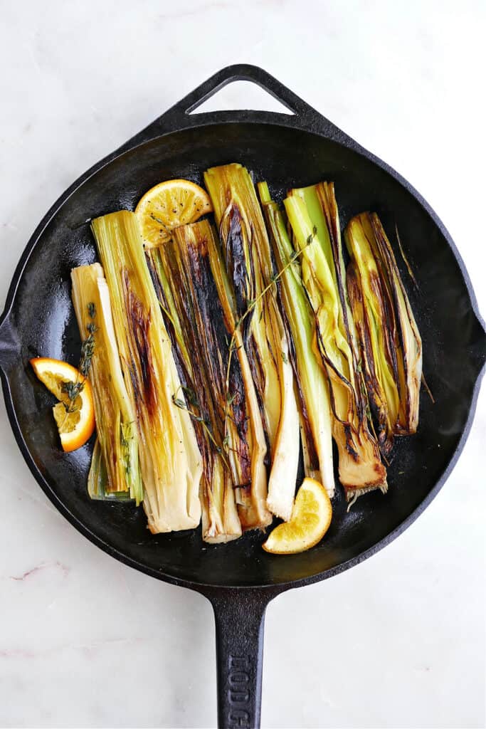 caramelized leeks in a cast iron skillet next to orange slices and thyme sprigs