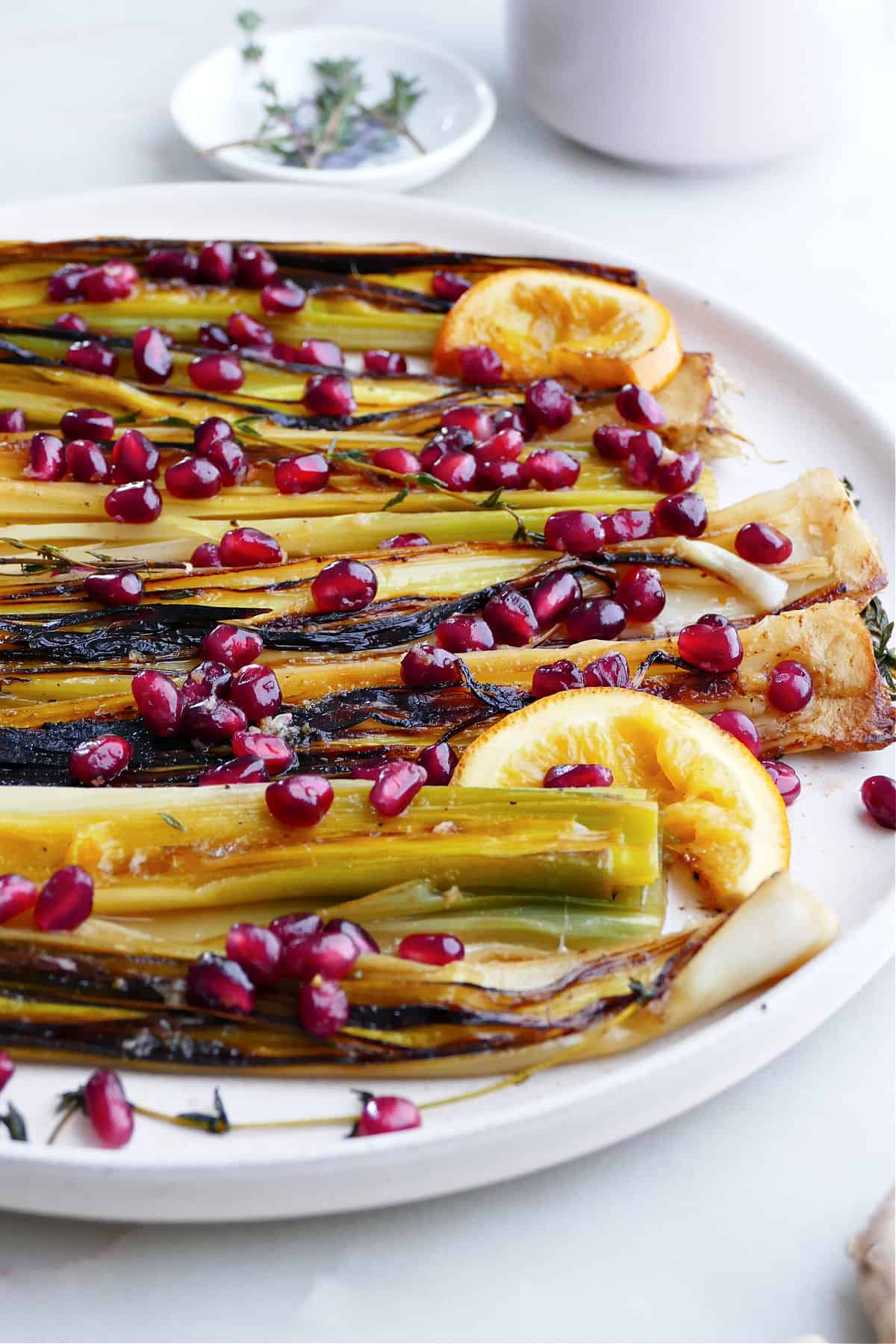 side angle of caramelized leeks on a platter topped with oranges and pomegranate arils