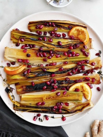square image of a platter with caramelized leeks topped with pomegranate arils and orange slices
