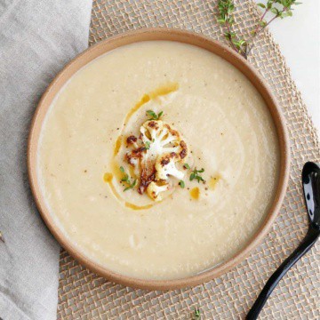 cauliflower and parsnip soup in a serving bowl topped with cauliflower, thyme, and oil