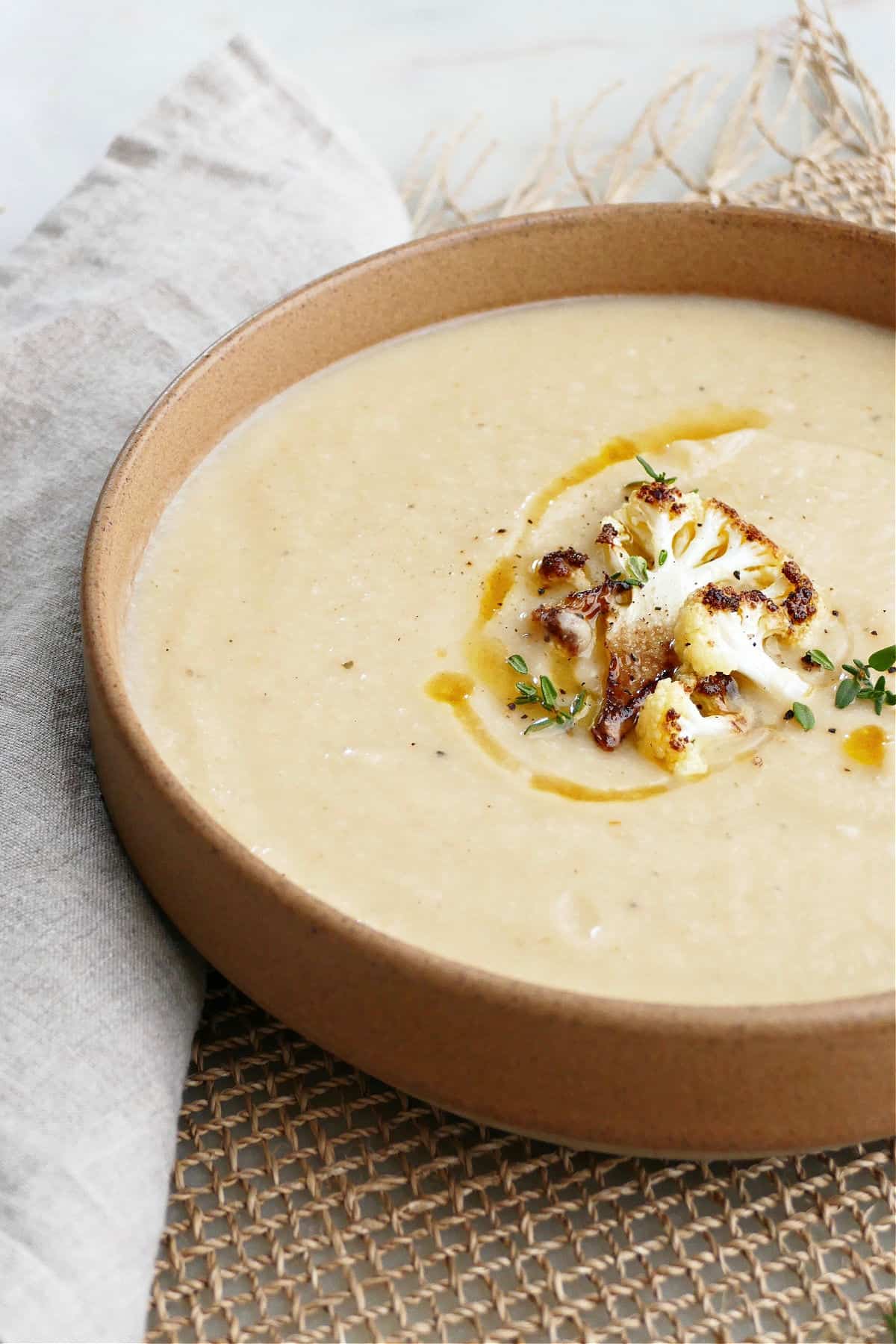 side view of vegan cauliflower and parsnip soup in a brown serving bowl with toppings