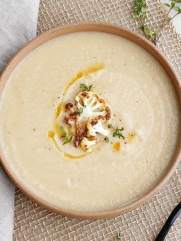 square image of creamy cauliflower parsnip soup topped with cauliflower, thyme, and oil