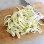 fennel sliced into half moon pieces on a cutting board with a knife