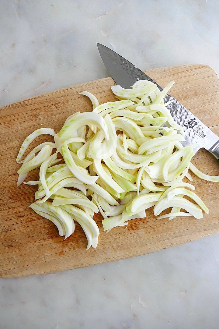 fennel sliced into half moon pieces on a cutting board with a knife