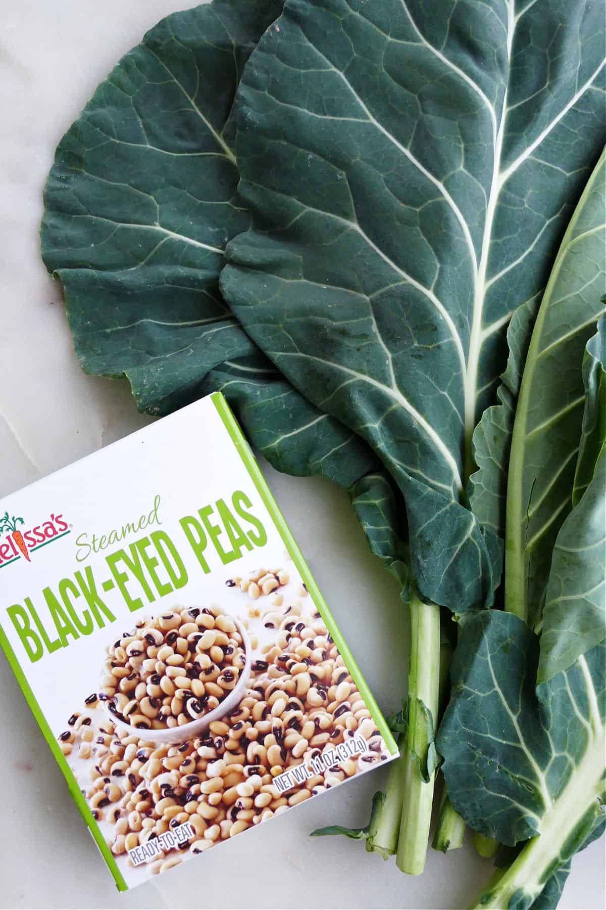 a box of steamed black eyed peas next to a bunch of collard greens on a counter