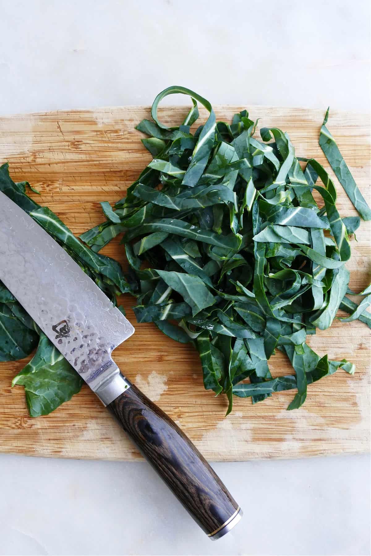collard greens sliced into ribbons on a cutting board next to a chef's knife