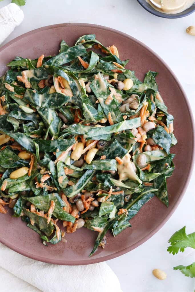 shredded collard greens, carrots, and peanuts with dressing on a brown serving dish