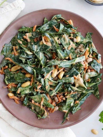 square image of collard greens salad with peanut sauce on a brown serving dish on a counter