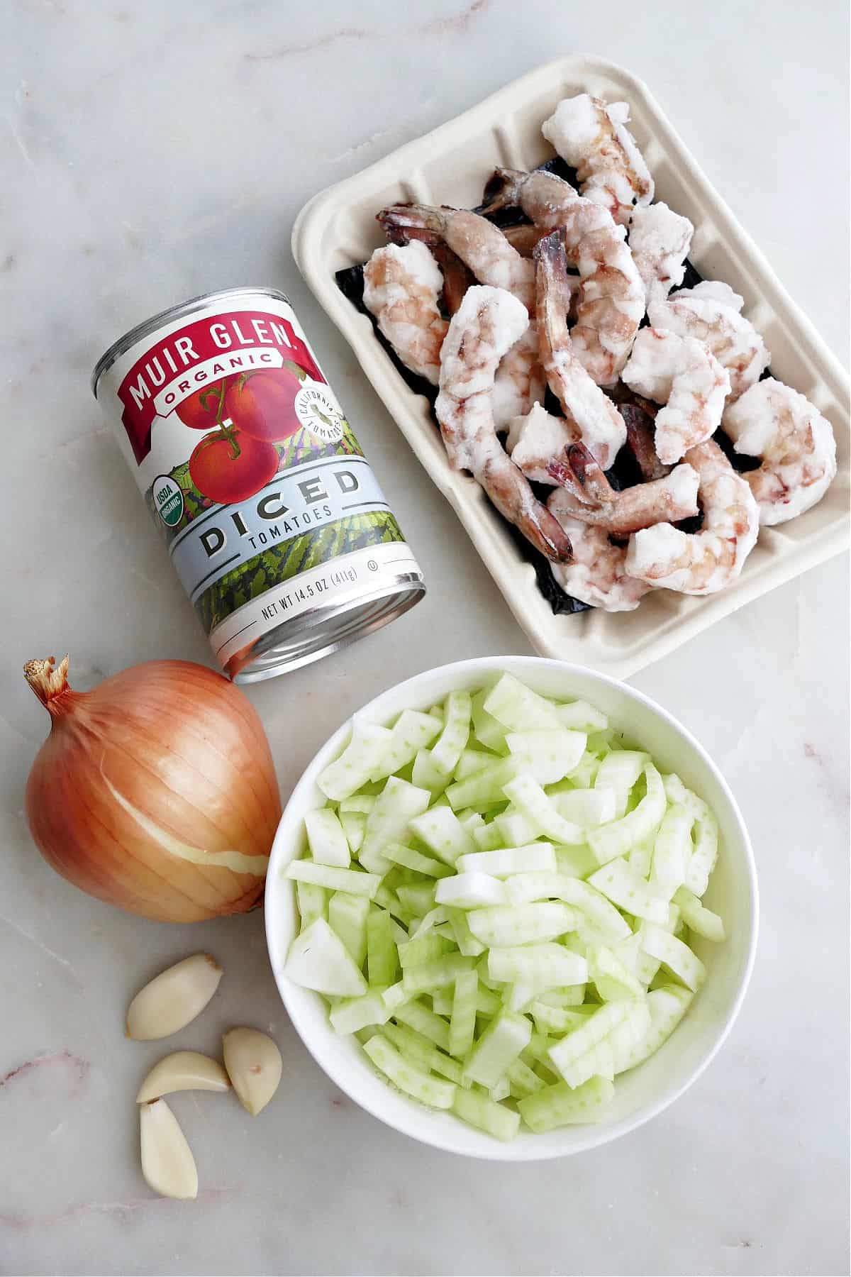 frozen shrimp, canned tomatoes, onion, garlic, and chopped fennel on a counter