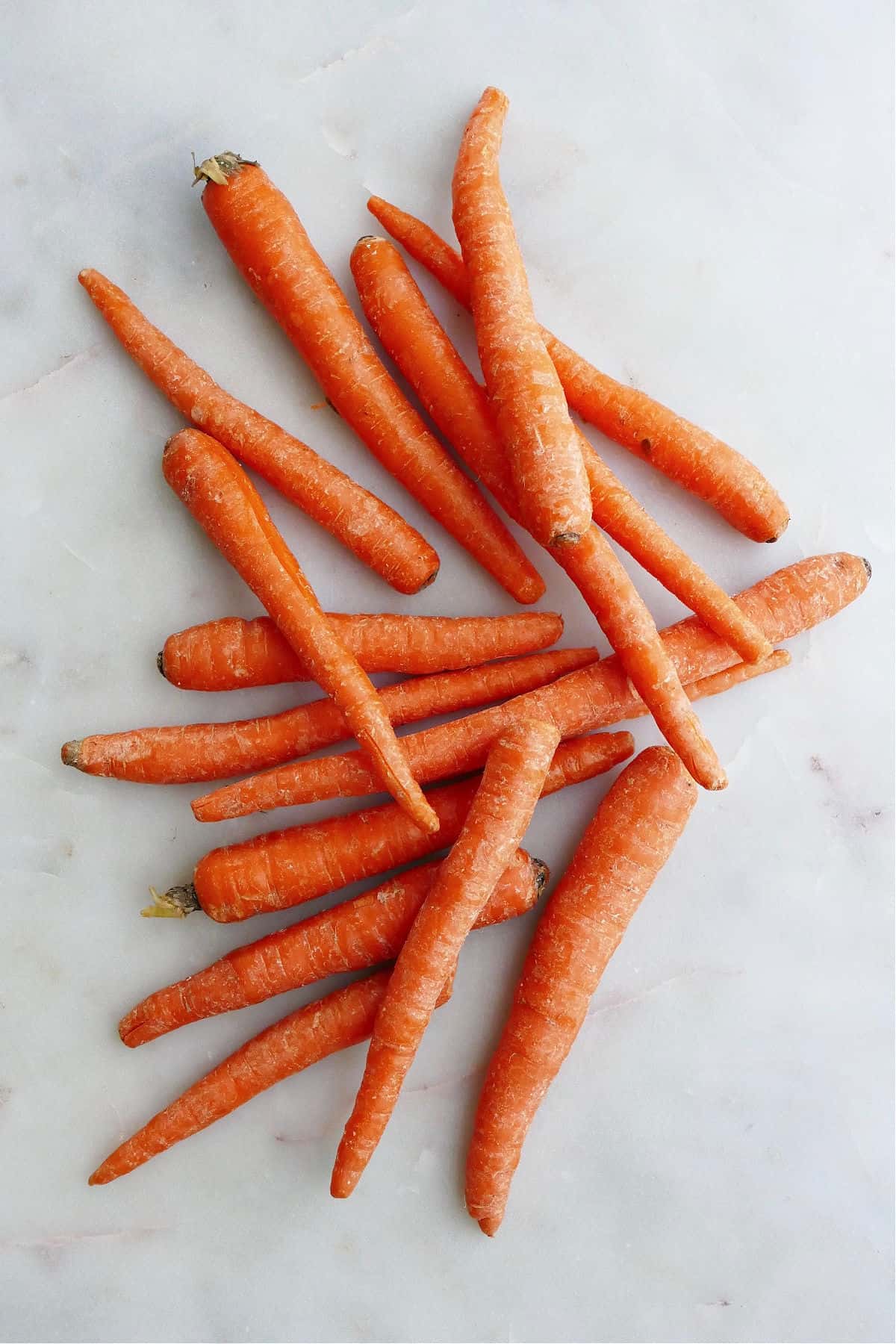  lange orange Karotten übereinander auf einer weißen Theke