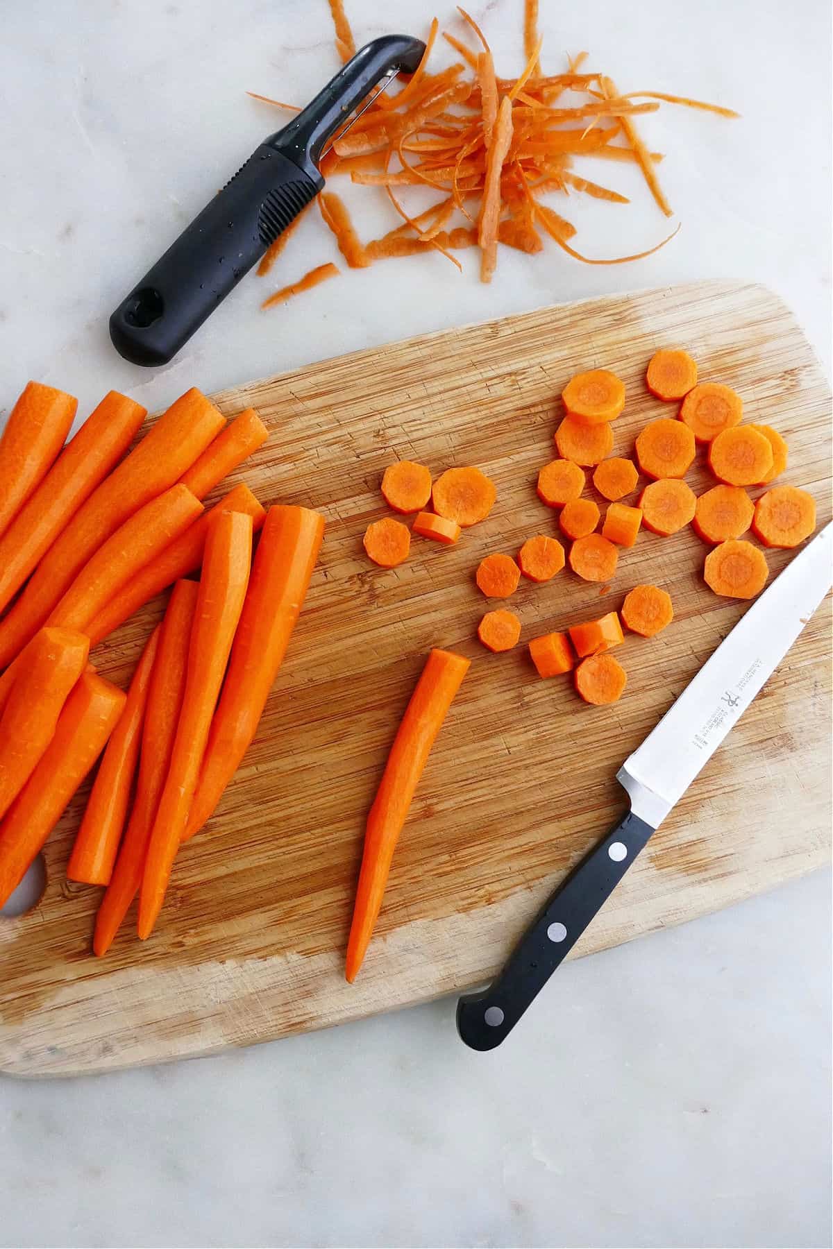 zanahorias peladas en una tabla de cortar junto a rodajas de zanahoria y peladuras