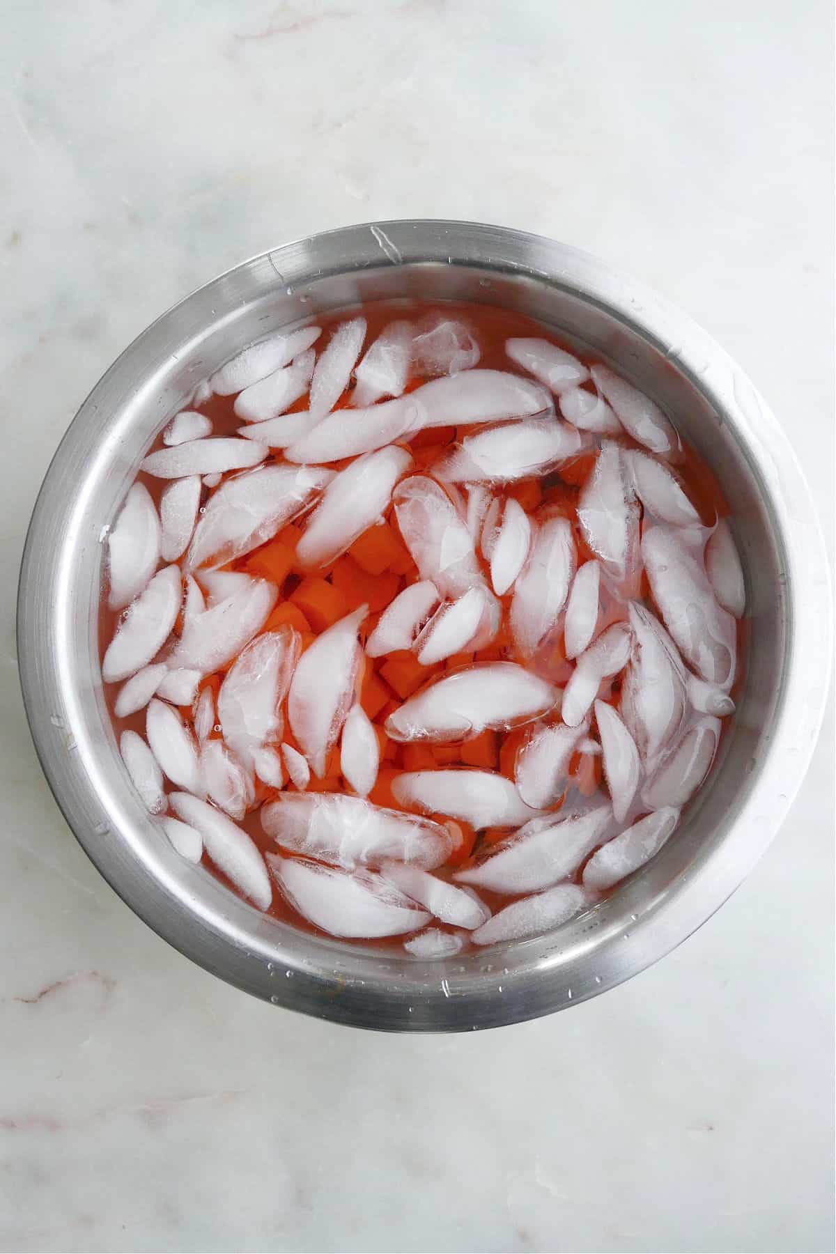cooked carrot coins in a bowl of ice water on a counter