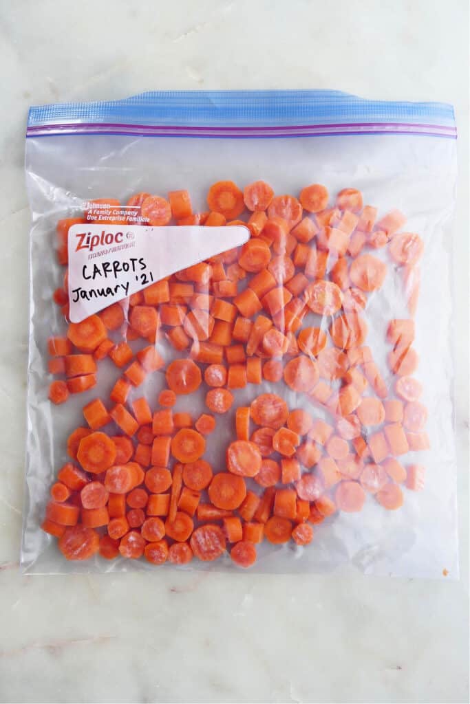 frozen carrot coins in a plastic bag labeled with the date on a counter