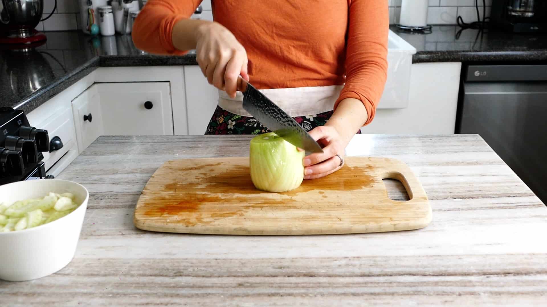 woman slicing a bulb of fennel in half using a chef's knife