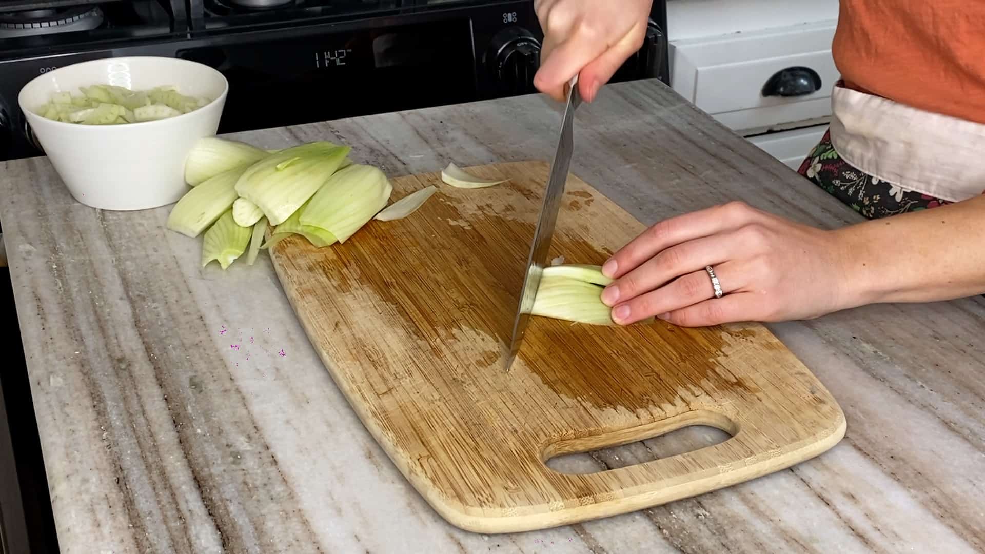 woman slicing a bulb of fennel with a chef's knife over a cutting board