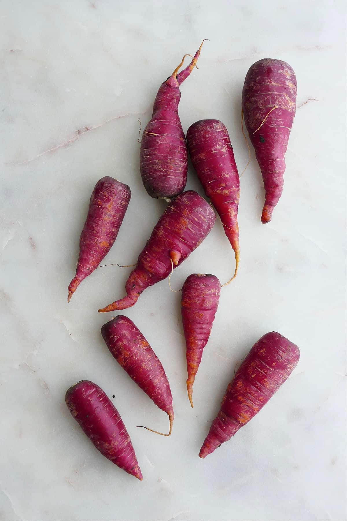 nine cosmic purple carrots spread out next to each other on a white counter