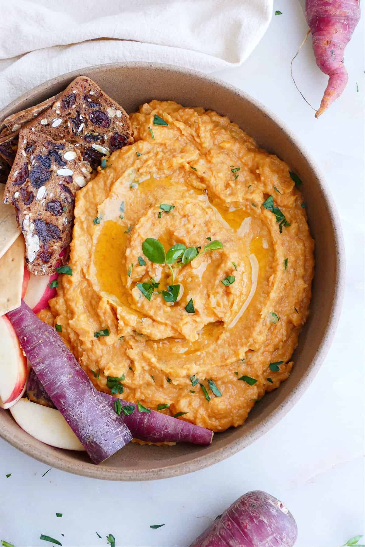 close-up image of carrot hummus in a serving dish with crackers and apples