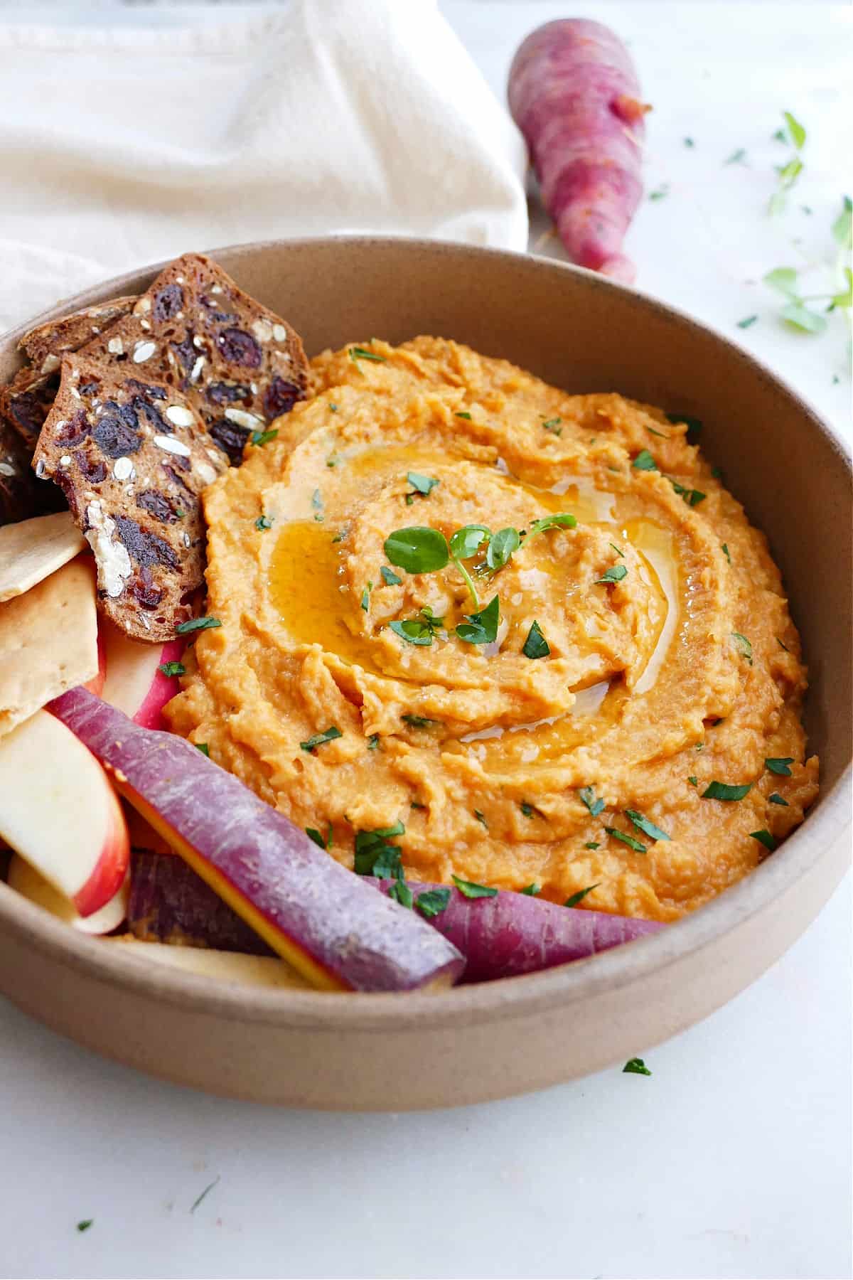 side angle of purple carrot hummus in a serving dish with crackers and apples