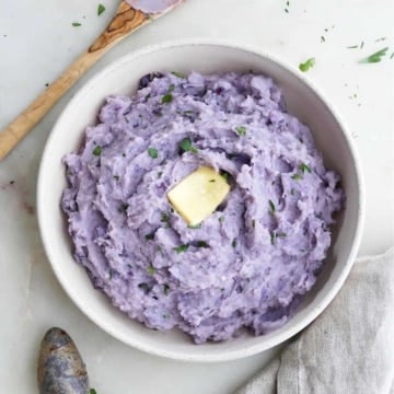 purple mashed potatoes topped with butter in a serving dish on a counter