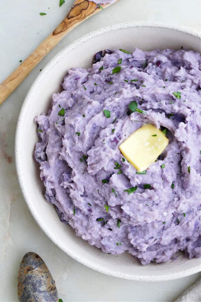 close-up image of purple mashed potatoes with butter and salt in a dish