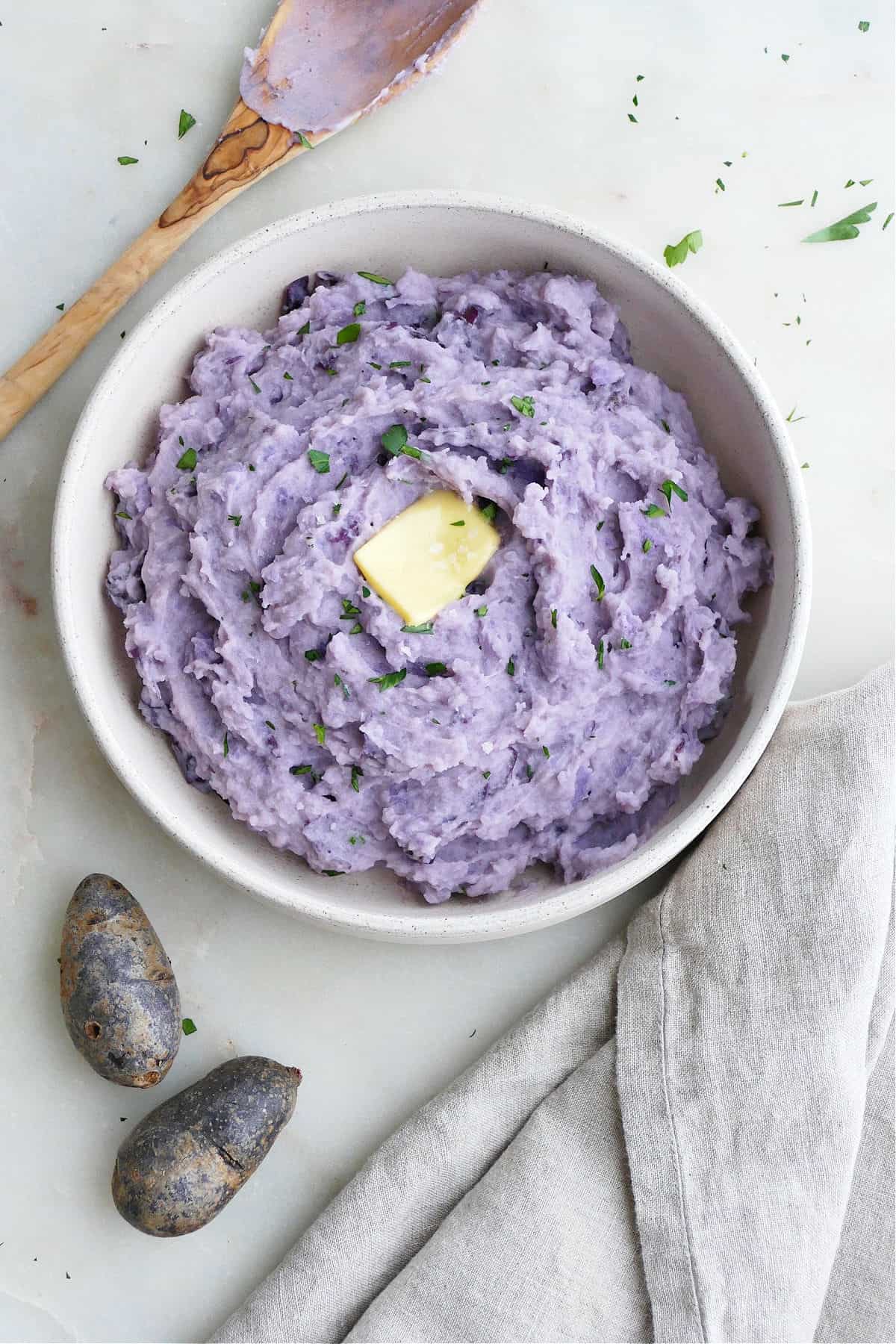 purple potatoes mashed in a serving bowl next to a napkin and whole potatoes