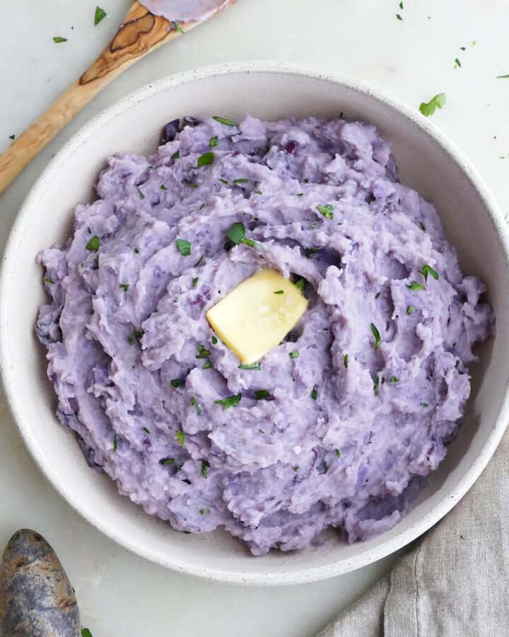 square image of purple mashed potatoes in a serving dish topped with butter