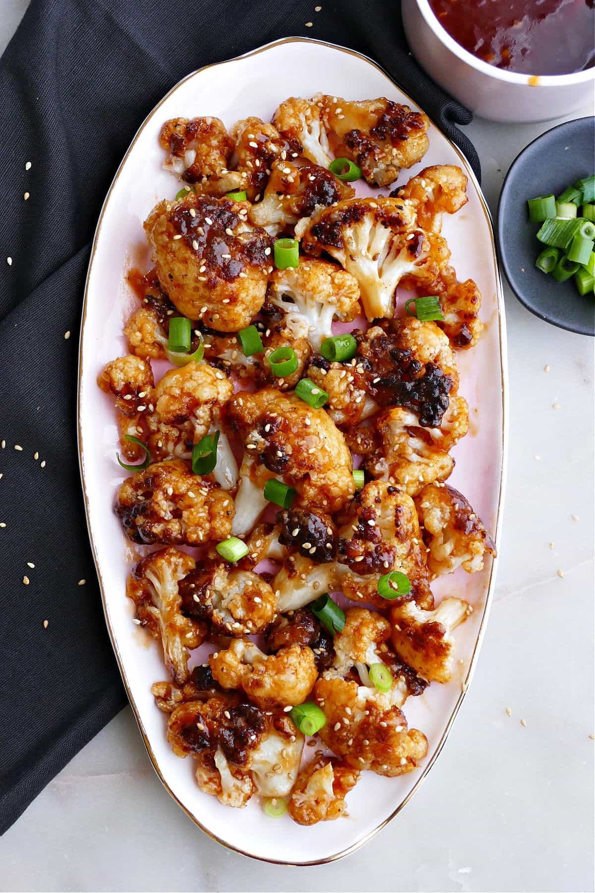 sweet and sour cauliflower on an oval serving dish next to a napkin and toppings