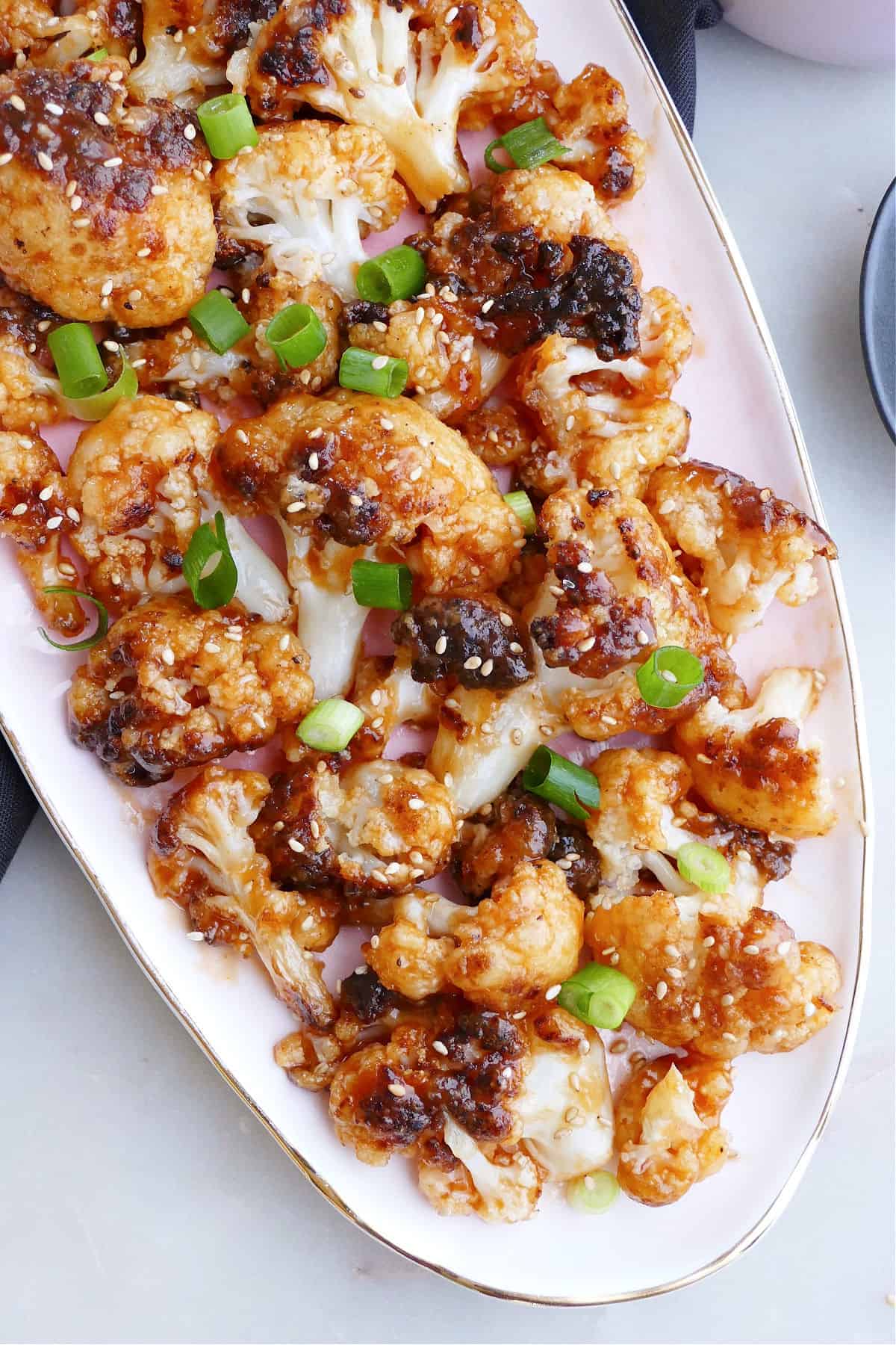 sweet and sour cauliflower on a serving tray topped with scallions and sesame seeds