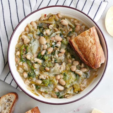 bowl of beans and escarole with bread on a napkin next to ingredients