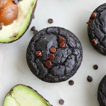 chocolate avocado muffin surrounded by avocados on a counter