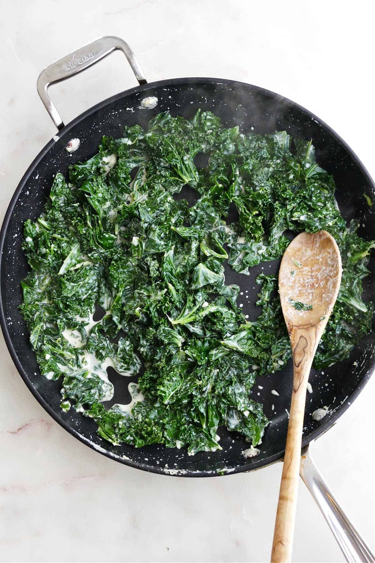 wilted kale cooking in a lemon garlic cream sauce in a skillet with a spoon
