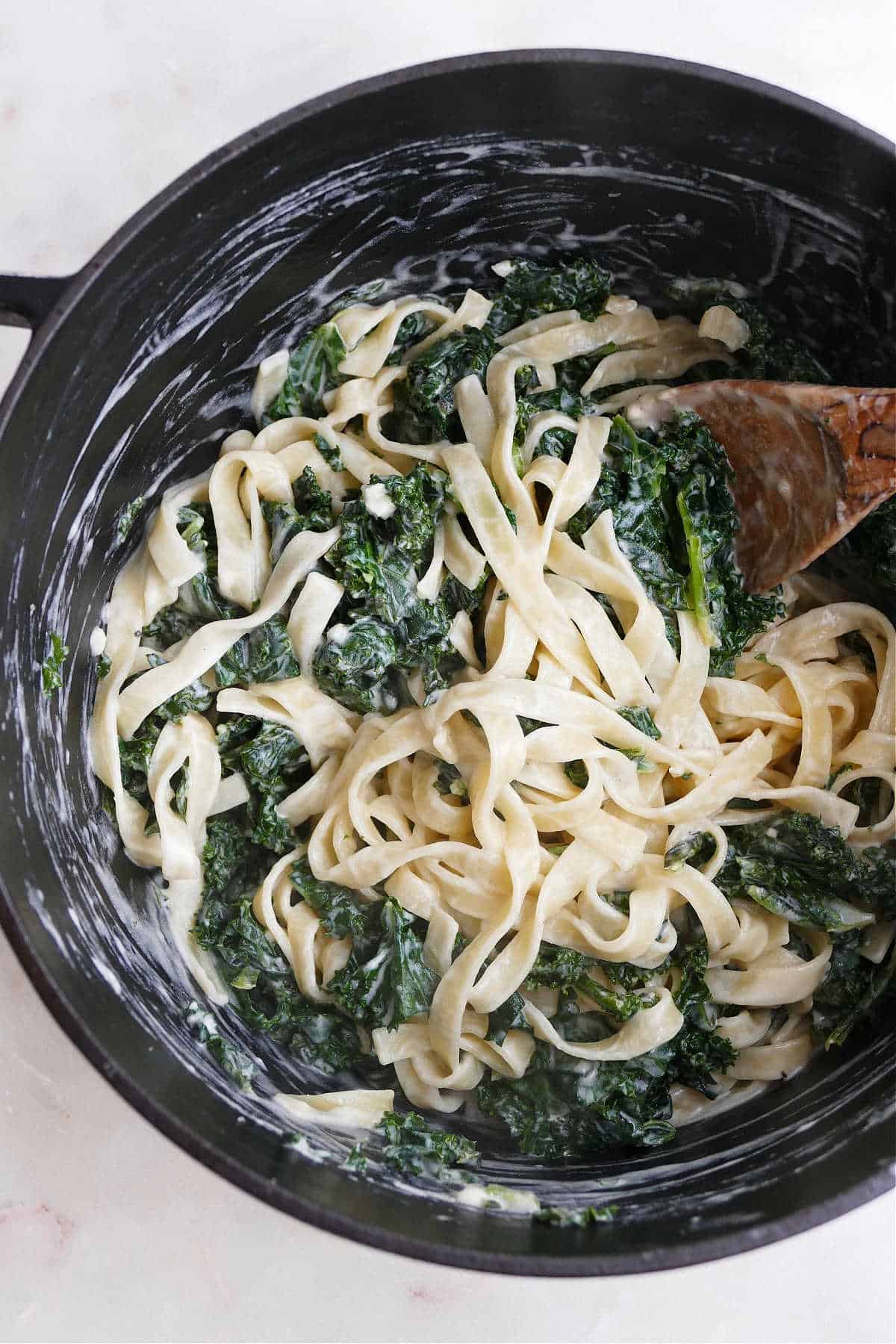 large pot of creamy kale pasta stirred with a wooden spoon on a counter