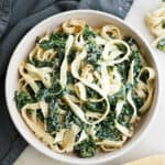 creamy kale pasta in a serving bowl on a napkin next to ingredients on a counter