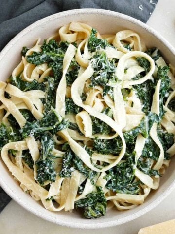 square image of creamy kale pasta in a serving bowl on a counter