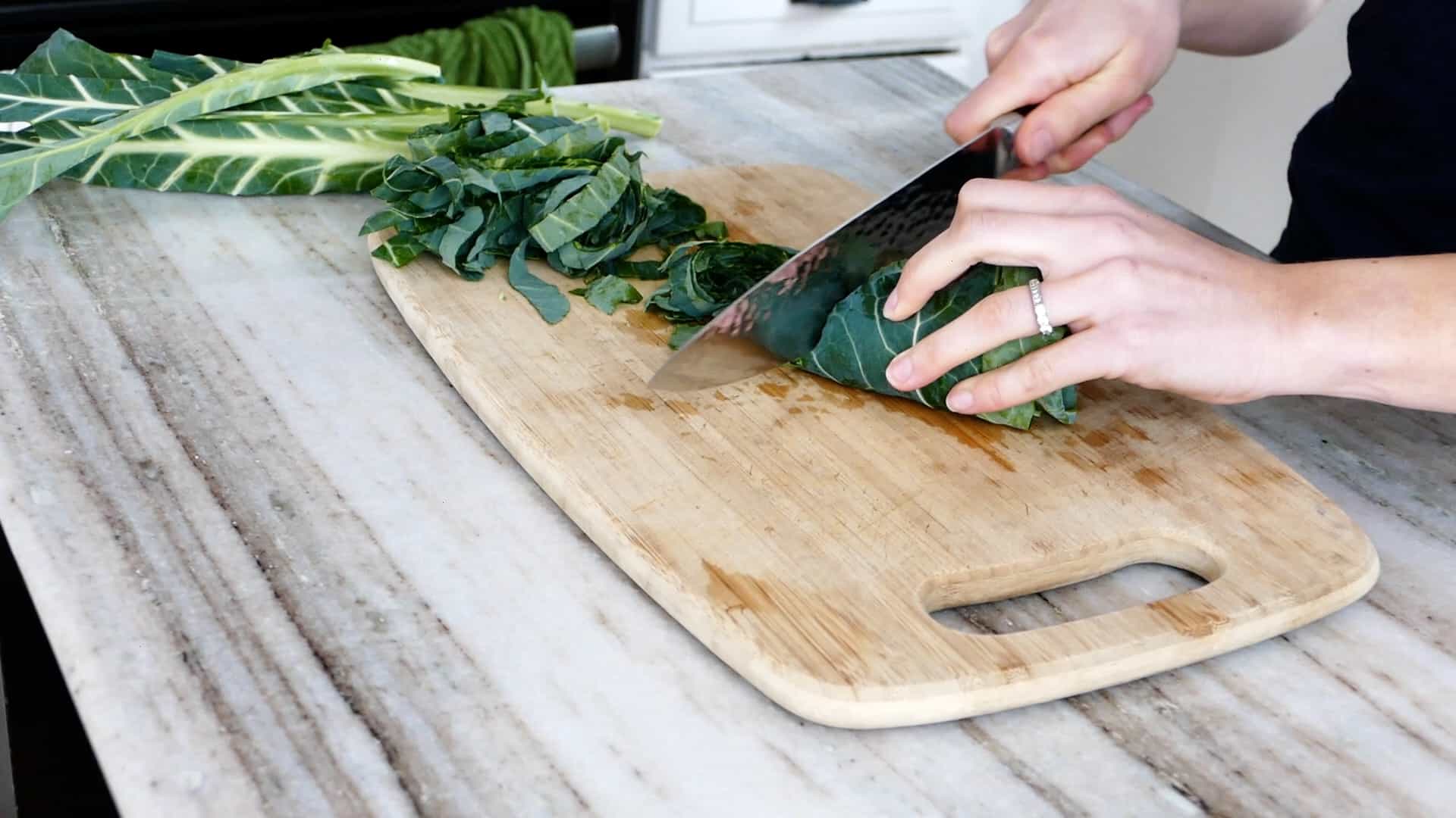 woman cutting collard greens into thin strips on a cutting board