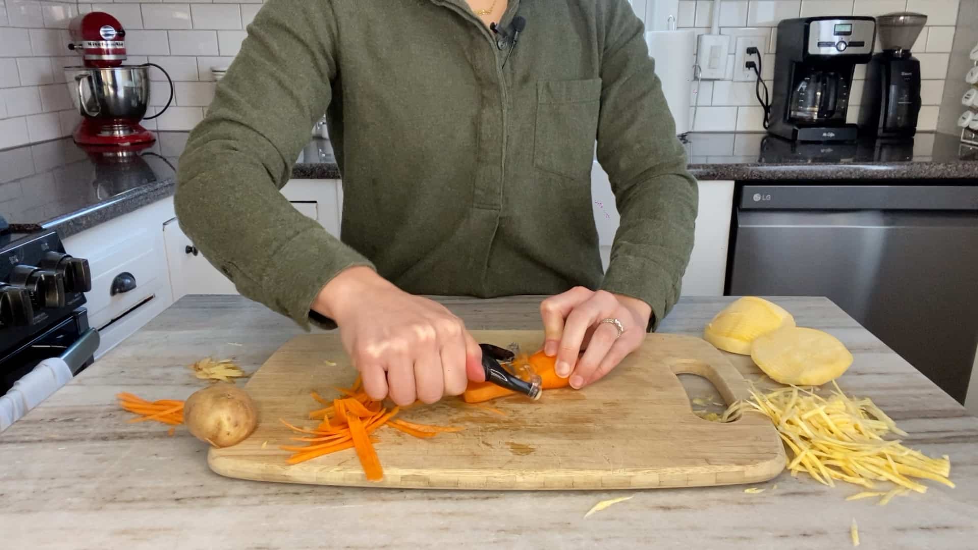 woman slicing a carrot with a julienne peeler on a bamboo cutting board