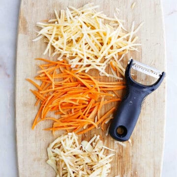 julienned vegetables on a cutting board next to an oxo peeler on a counter