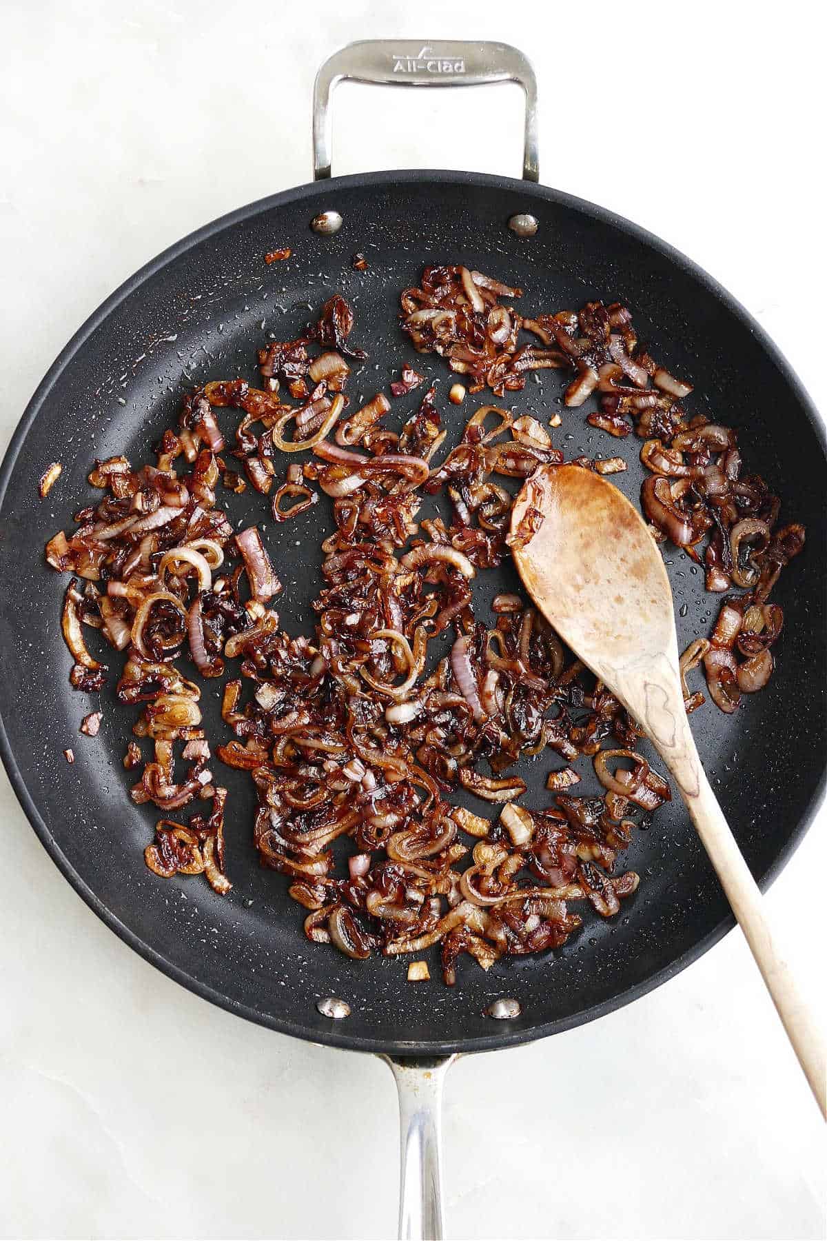 balsamic caramelized shallots in a large black skillet with a wooden spoon